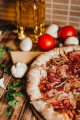 A piece of pizza with sausages in the background cheese, tomatoes, garlic, mashrooms and olive oil with a transparent bottle on a wooden table