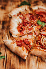 Clice of pizza with pepperoni and salami on a rustic wooden table.