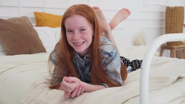 Happy ginger girl smiling on cozy bed at home