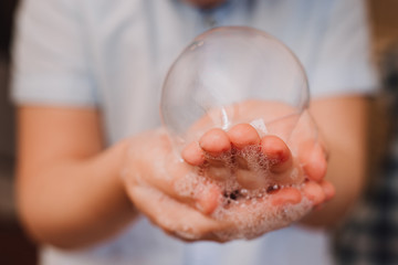 Little boy playing blowing and making soap bubbles holding bubble in his hand