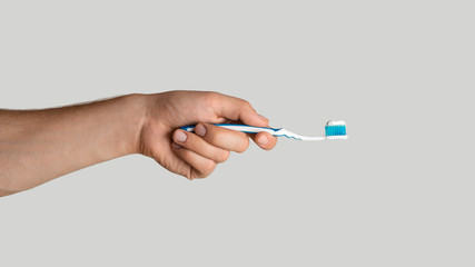 Oral hygiene. Young guy holding toothbrush with paste on light grey background, closeup. Panorama