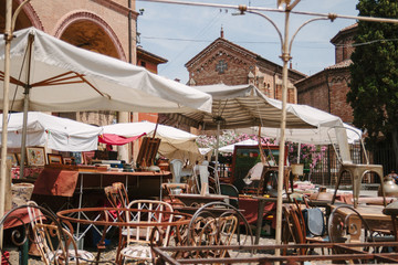 Flea market in Bologna. Old unnecessary things sell in the street. Italian flea market in sunny day. Ancient building with arch. Square with tables and chairs. Ancient furniture on the bazaar. Nobody.
