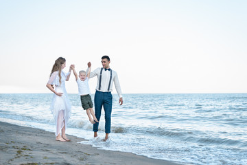 Walking along the sea shore. Wide view of mom, dad and son walking in sea