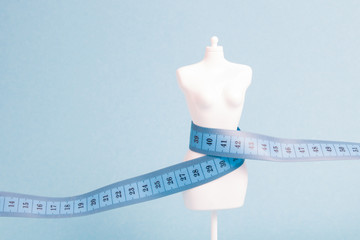 white mannequin wrapped in blue measuring tape, blue background, weight loss concept, copy space,...