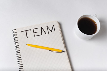Handwritten word TEAM. Inscription in notebook. Mug with coffee on white background.