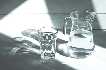 A glass of clean clear water stands on a white wooden background with sharp shadows