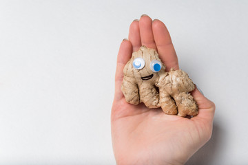 Ginger with funny face and Googly eyes lying on palm hand. White background.