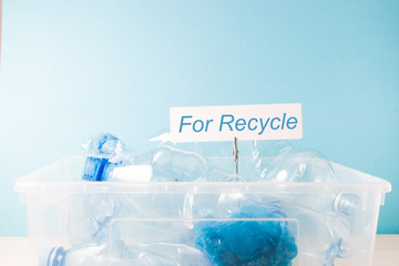 white rectangular cardboard label on a clothespin on a paper spring in a plastic waste container, waste recycling and waste sorting concept, blue background, copy space