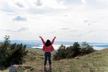 a girl with her arms outstretched in nature on the background of a lake next to fir trees