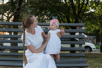 Fototapeta premium Young happy mother playing with baby girl sitting on bench in Park