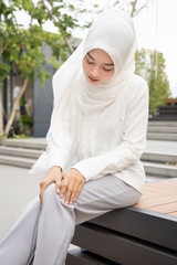 woman with knee joint pain; muslim woman with hand holding injured knee; portrait of asian woman...
