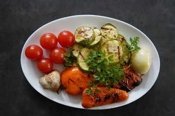 Plate with grilled vegetables - pepper, zucchini, onions, grill on a gray background