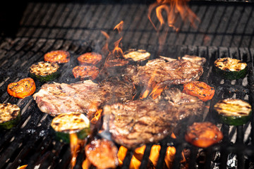 Meat and vegetables cooking on a barbecue. The flames from the fire cover the meat.