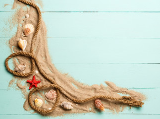 Sea rope with many different sea shells on the sea sand on a blue wooden background. Top view.