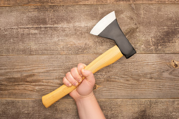 partial view of man holding axe on wooden surface