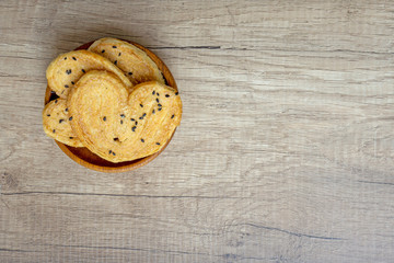 Brown crispy bread crunchy butterfly puff with black sesame seeds topping in wooden bowl on grey wooden table, top view angle of shooting and copy space
