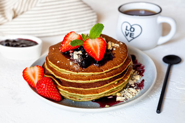 Pancakes with strawberries, jam, nuts an mint. Breakfast with pancakes and black coffee, top view