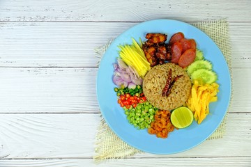 Rice seasoned with shrimp paste served with various side dishes on white wooden table, deliciously authentic Thai food.