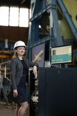 Portrait of a female factory manager in a white hard hat and business suit. Controlling the work process at the airplane manufacturer.