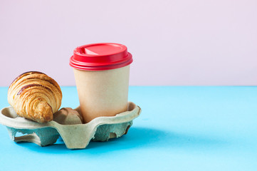 Disposable cup of coffee and croissant in a container.