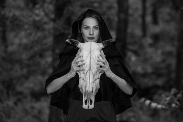 Victim with skull of the animal instead of head. Photo stylized as shooting on an old camera, with noise and imperfection of the image. Woman in forest with skull of cow occupies Occult calls to demon