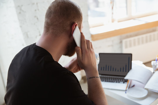Young man studying at home during online courses for analytics, financists, economists. Getting profession while isolated, quarantine against coronavirus spreading. Using laptop, smartphone, devices.