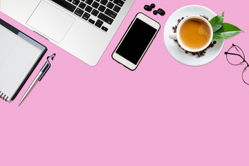 Top view of pink office desk table with laptop, smartphone, coffee cup, notebook, glasses with copy space.