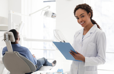 Smiling female dentist filling medical form in cabinet