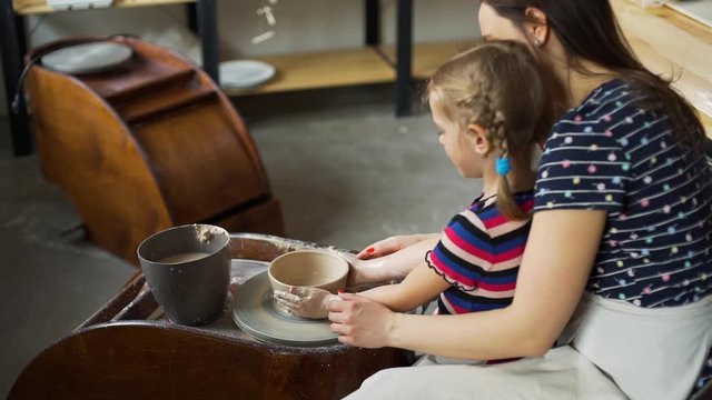 Young Mother with her Cute Little Girl Shaping Clay Together while Working on a Pottery Wheel. Concept of Art, Handmade Crafts, Hobby and Activities for Children