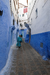 Unrecognized women walking down the ancient street in kasbah - old part of city Chefchaouen, Morocco.