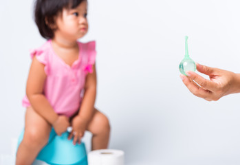 Asian little cute baby child girl training to sitting on blue chamber pot or potty her problem cannot shit and mother use Enema for help, studio shot isolated on white background, wc toilet concept