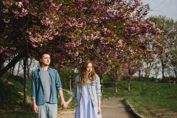 Romantic and happy caucasian couple in casual clothes hugging on the background of beautiful blooming trees. Love, relationships, romance, happiness concept. Man and woman walking outdoors together.