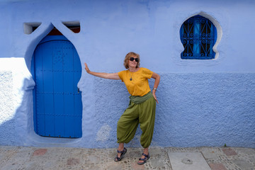 Pretty woman funny posing near the facade of an old house in the blue city of Chefchaouen, Morocco.