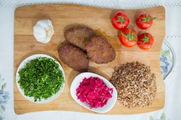 Meat cutlets, baked buckwheat on a wooden board . Red cabbage sauerkraut . Garlic, Onion, Tomatoes. Chopped coriander. Homemade cutlets with oatmeal on a table . Meat cutlets on a wooden skewer .