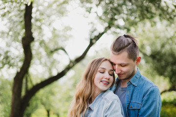 Romantic and happy caucasian couple in casual clothes hugging on the background of beautiful blooming trees. Love, relationships, romance, happiness concept. Man and woman walking outdoors together.