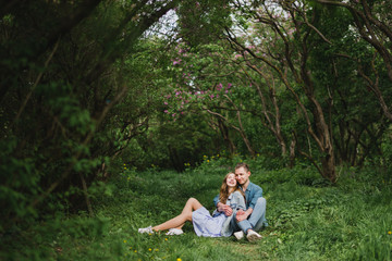 Romantic and happy caucasian couple in casual clothes hugging on the background of beautiful blooming lilac. Love, relationships, romance, happiness concept. Man and woman walking outdoors together.