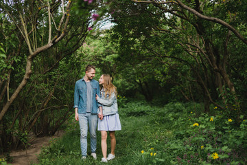 Fototapeta premium Romantic and happy caucasian couple in casual clothes hugging on the background of beautiful blooming lilac. Love, relationships, romance, happiness concept. Man and woman walking outdoors together.