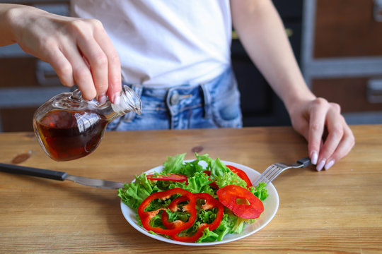 Girl adds oil to salad, use of olive oil in diet