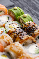 Sushi with salmon and tuna, avocado and cucumber, cheese, sesame and caviar on a black stone sushi board.