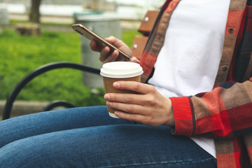 Woman drink coffee and uses smartphone in park. Lunch break