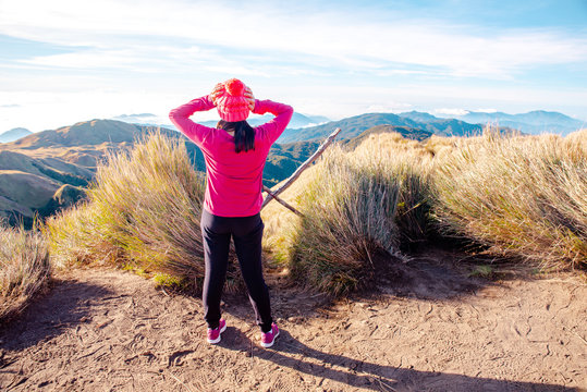 An adult female in in pink shirt standing at the peak of Mt. Pulag National Park enjoying the breathtaking view of the sea of clouds