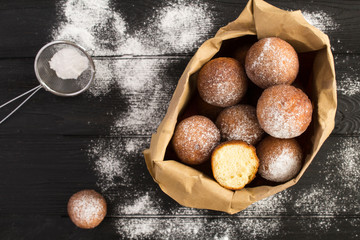 Homemade cottage cheese donuts in the paper package  on the black wooden background. Top view....