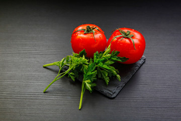 Two beautiful appetizing tomatoes and parsley leaves on a dark background. Health food. Vegetables on a wooden table. Red-green beautiful picture. Ingredients for a delicious salad. Drops of water 