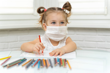 Little girl 4 years old in a disposable mask draws with pencils at home at the table