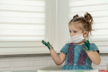 Little girl in mask paints with fingers