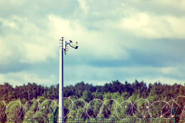 Obraz premium Fence, barbed wire and video camera. Obstruction and surveillance observation.