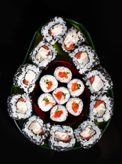 Japanese sushi food. Maki rolls and uramaki with tuna, salmon, caviar and cucumber. Sushi laid out in avocado shape on black background.