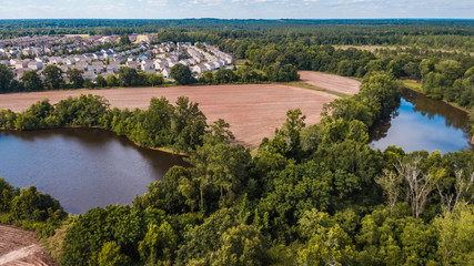 Fototapeta na wymiar Aerial view of farmland fields and two ponds surrounded by a forest next to a residential subdivision with many houses
