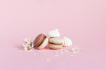 Tasty french macarons, marshmallows and spring blossom on a pink pastel background.
