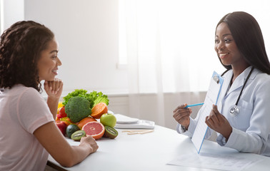Black lady nutritionist showing female patient medical chart